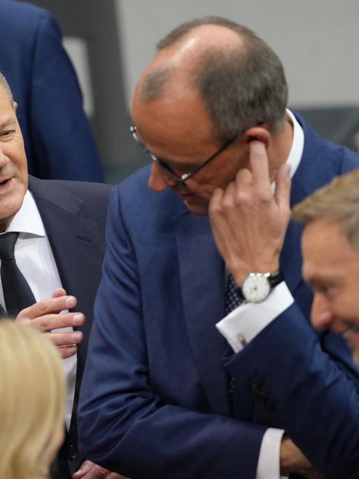 Bundeskanzler Olaf Scholz (SPD, l) spricht im Plenum des Bundestags vor seiner Regierungserklärung mit Friedrich Merz (M), CDU-Bundesvorsitzender und Unionsfraktionsvorsitzender.