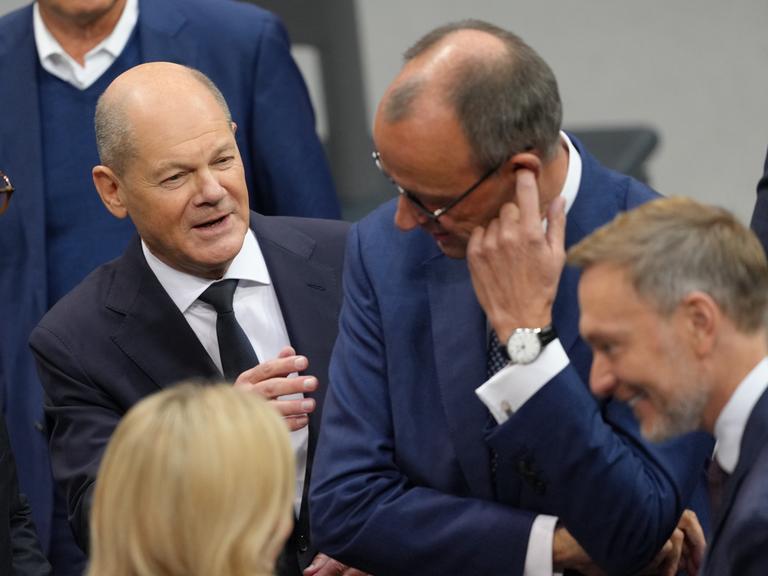 Bundeskanzler Olaf Scholz (SPD, l) spricht im Plenum des Bundestags vor seiner Regierungserklärung mit Friedrich Merz (M), CDU-Bundesvorsitzender und Unionsfraktionsvorsitzender.