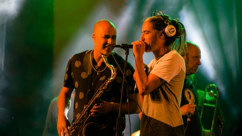 Der Sänger und der Saxophonist der Band stehen einander zugewandt auf der Bühne.