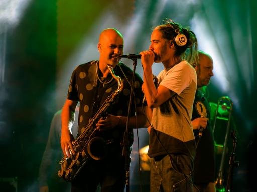 Der Sänger und der Saxophonist der Band stehen einander zugewandt auf der Bühne.
