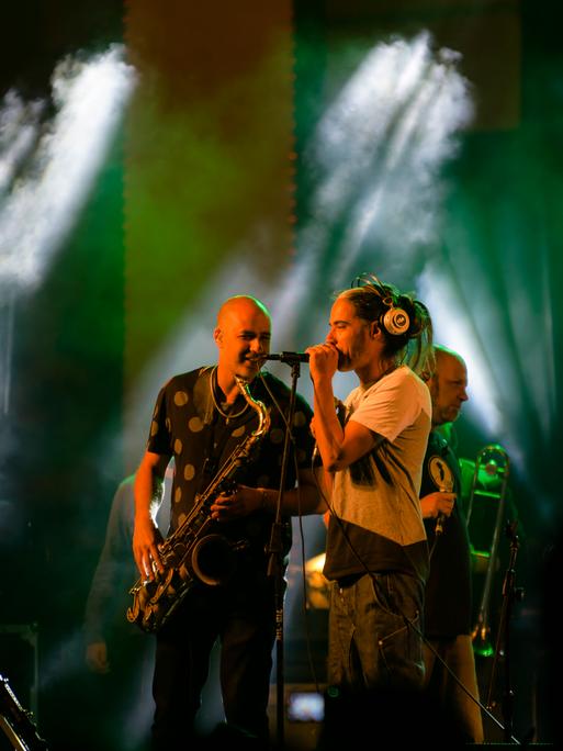 Der Sänger und der Saxophonist der Band stehen einander zugewandt auf der Bühne.