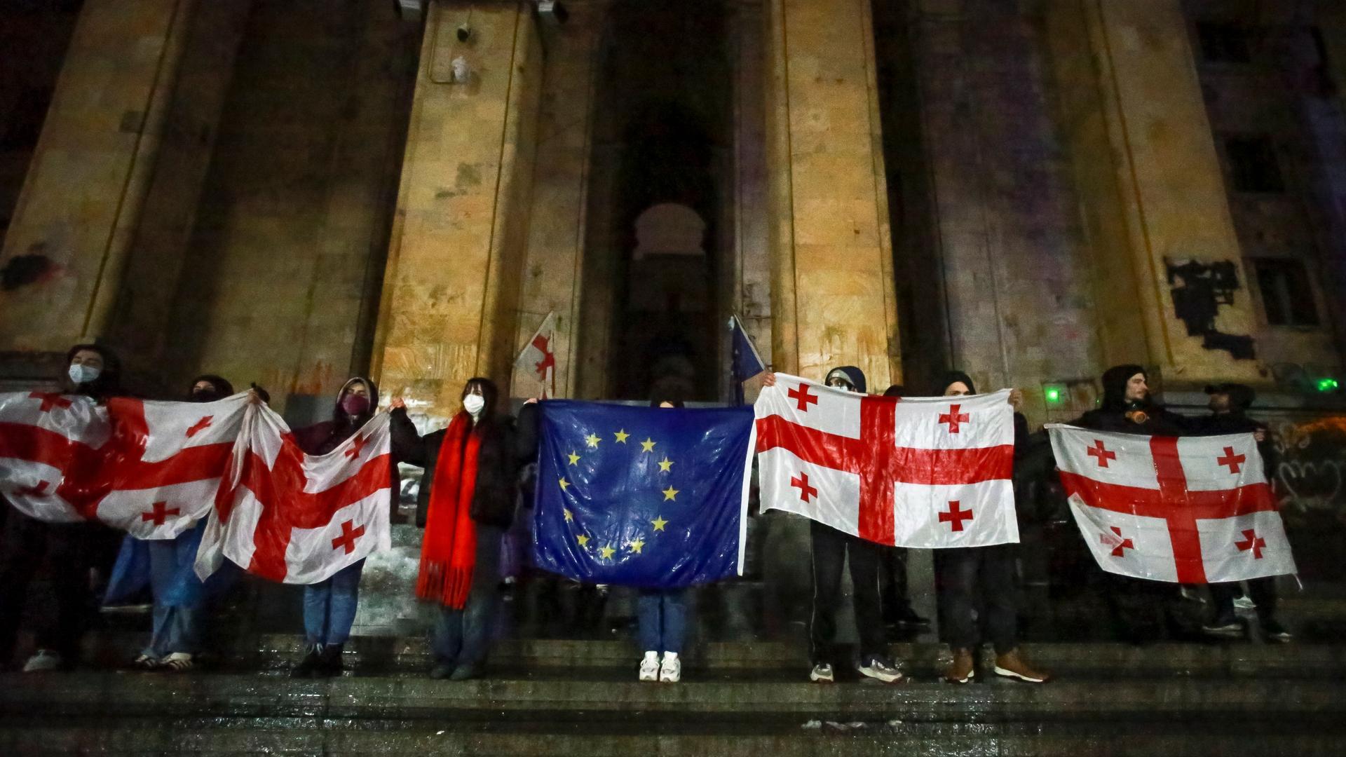 Demonstranten halten eine EU-Flagge und georgische Nationalflaggen  vor dem Parlamentsgebäude in der georgischen Hauptstadt Tiflis.