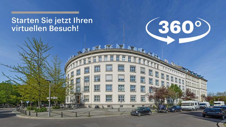 Ein mehrstöckiges, weißes Eckgebäude in einer Panoramaaufnahme vor blauem Himmel.