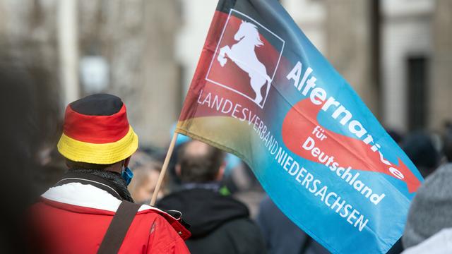 Bei einer Demonstration trägt ein Teilnehmer eine Fahne des niedersächsischen Landesverbandes der Partei AfD.