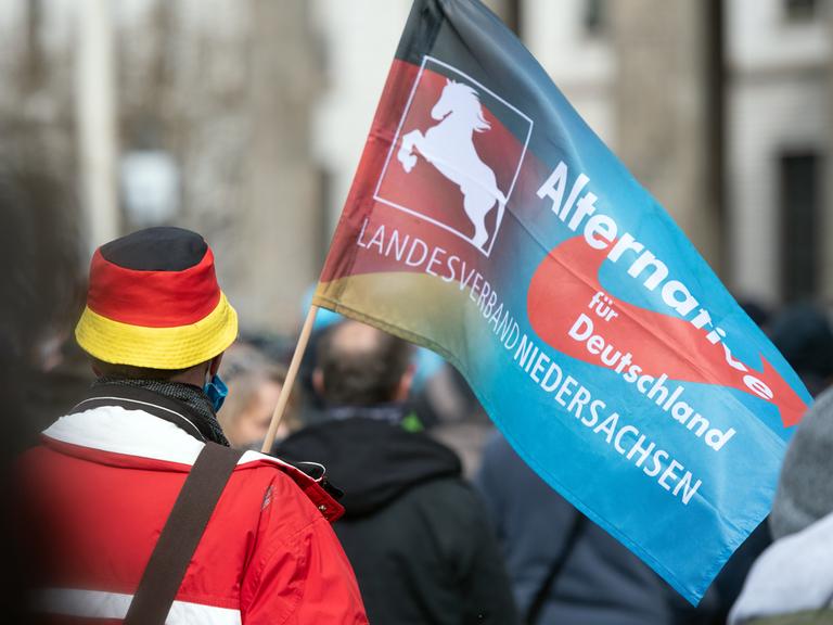 Bei einer Demonstration trägt ein Teilnehmer eine Fahne des niedersächsischen Landesverbandes der Partei AfD.