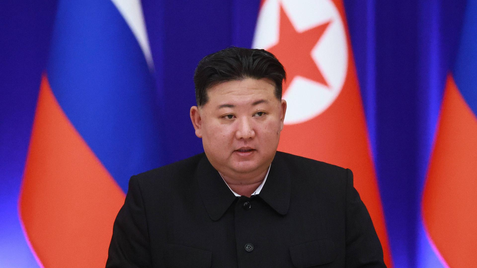 Porträt von Kim Jong Un mit der nordkoreanischen und der russischen Flagge im Hintergrund.