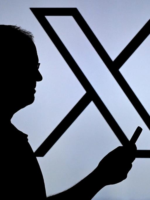 Ein Mann blickt auf sein Handy, im Hintergrund ist ein großes X zu sehen. Ein Mann blickt auf sein Handy, im Hintergrund ist ein großes X zu sehen.