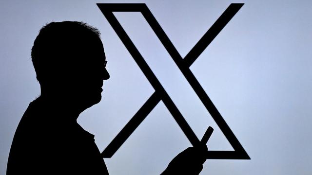 Ein Mann blickt auf sein Handy, im Hintergrund ist ein großes X zu sehen.