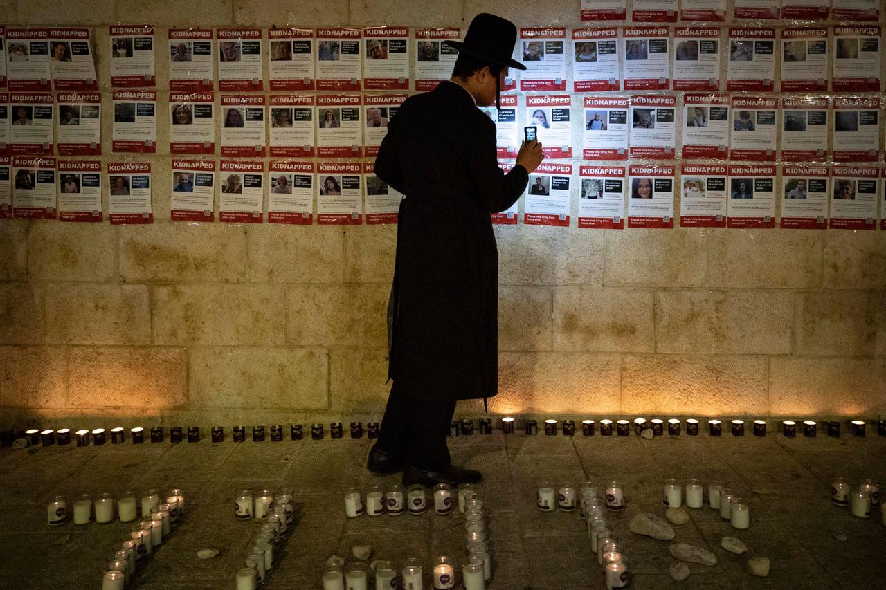 Ein Mann steht vor Fotos von vermissten Geiseln in Jerusalem.