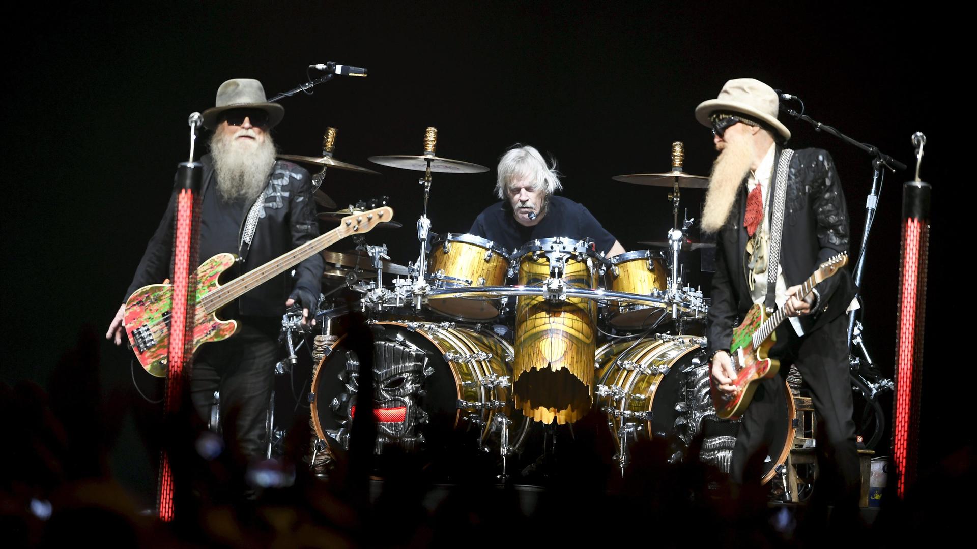 Die Band ZZ Top bei einem Auftritt in Helsinki: Rechts und links ein Mann mit langem Bart und einer E-Gitarre. In der Mitte sitzt ein dritter Mann an einem Schlagzeug, ohne Bart.