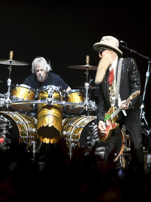 Die Band ZZ Top bei einem Auftritt in Helsinki: Rechts und links ein Mann mit langem Bart und einer E-Gitarre. In der Mitte sitzt ein dritter Mann an einem Schlagzeug, ohne Bart. Die Band ZZ Top bei einem Auftritt in Helsinki: Rechts und links ein Mann mit langem Bart und einer E-Gitarre. In der Mitte sitzt ein dritter Mann an einem Schlagzeug, ohne Bart.