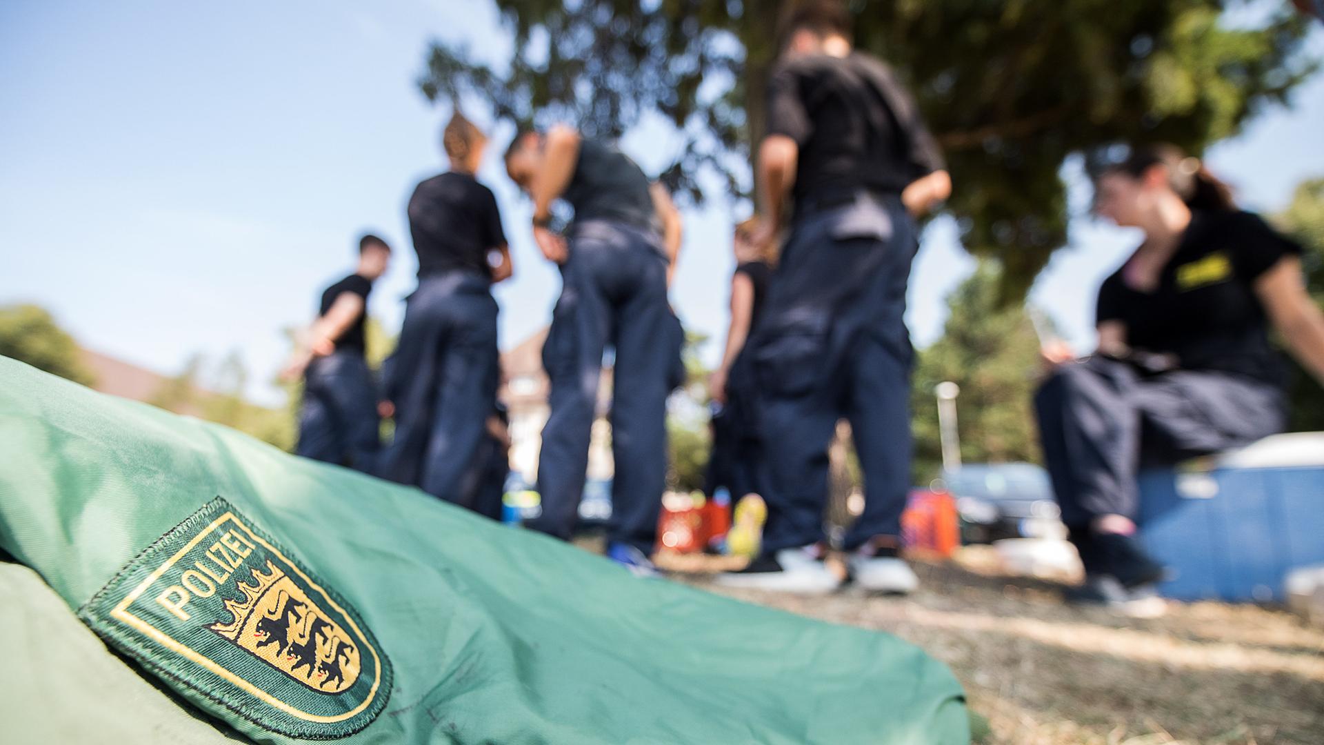 Eine Jacke mit dem Logo der Polizei Baden-Württemberg liegt auf dem Gelände der 5. Bereitschaftspolizeiabteilung Böblingen auf dem Boden. Im Hintergrund sind schemenhaft Menschen zu sehen. Hier testen Schüler Fitness und Konzentrationsfähigkeit.