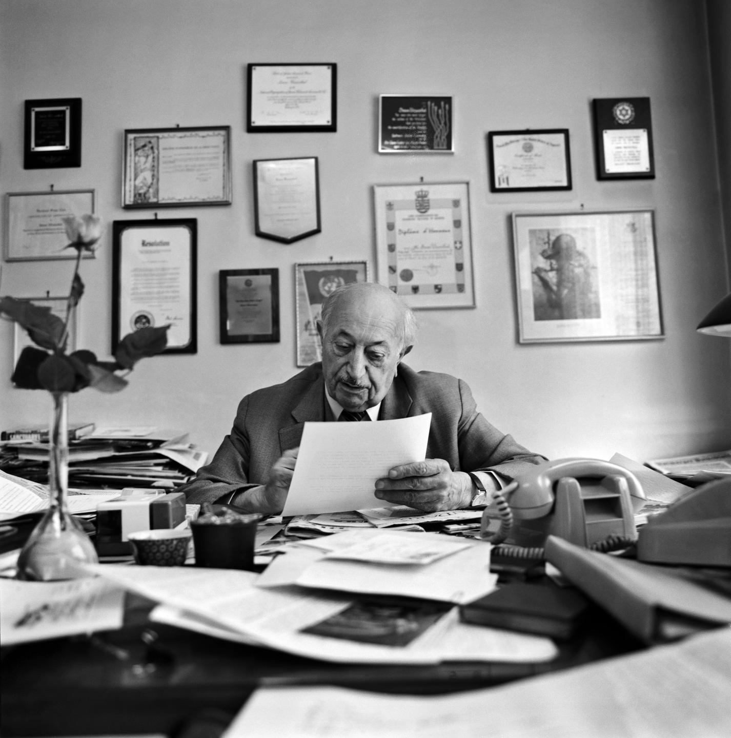 Der Schriftsteller und Publizist Simon Wiesenthal (1908 - 2005) in seinem Büro in Wien. Er blickt auf Unterlagen, im Hintergrund hängen gerahmte Fotos. 
