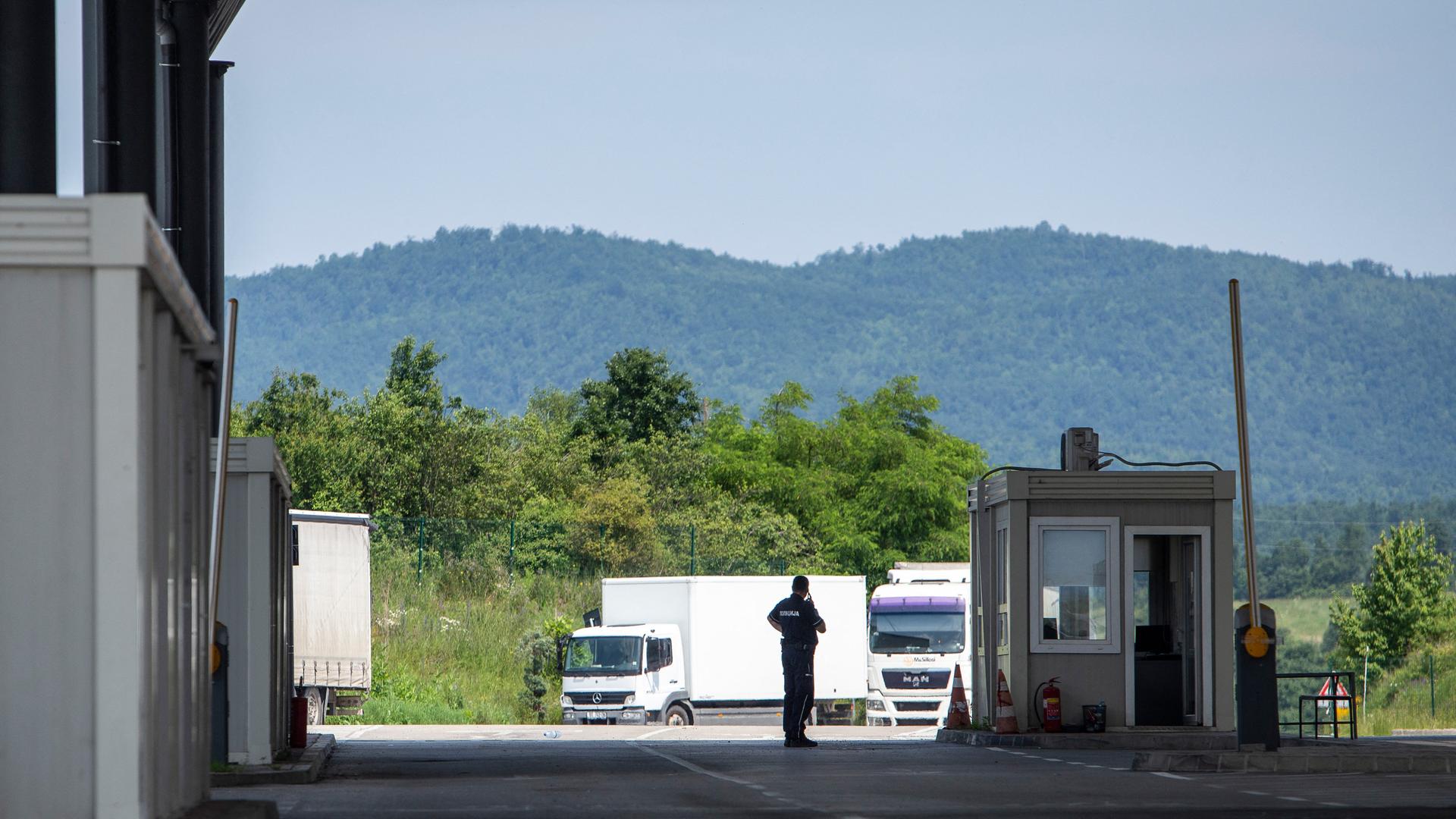 Ein Polizist steht am Grenzübergang Merdare zwischen Serbien und dem Kosovo. Im Hintergrund sind zwei LKW zu sehen. 