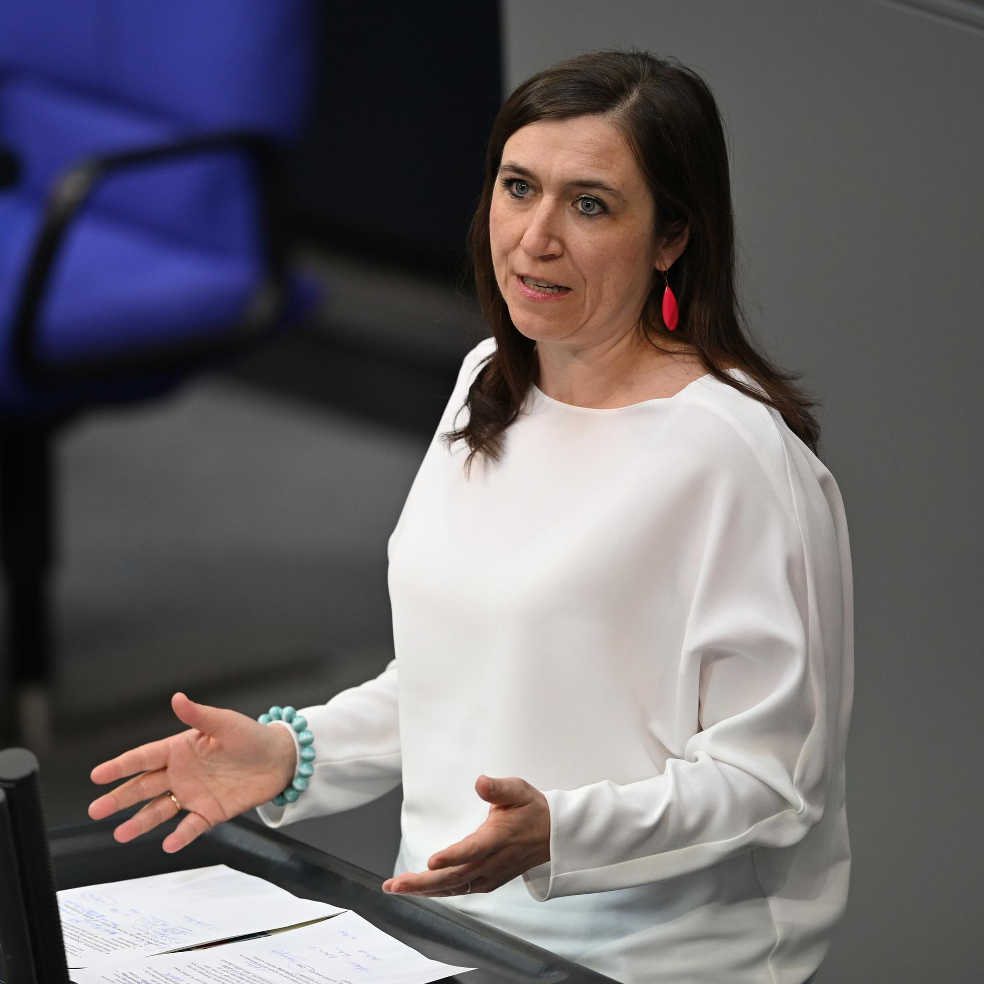Katharina Beck steht an einem Rednerpult und spricht, sie trägt ein weißes Oberteil.