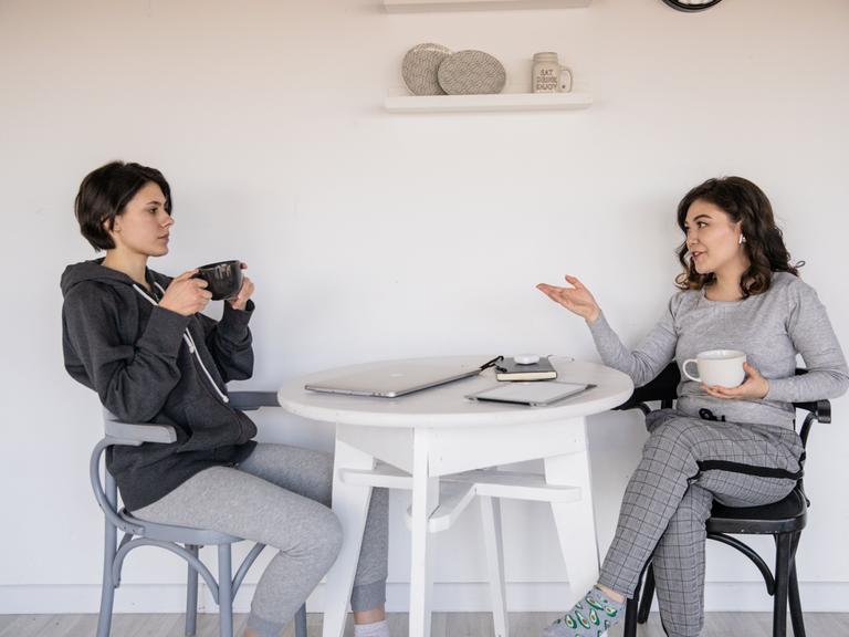 Zwei Frauen sitzen an einem Tisch und unterhalten sich. 