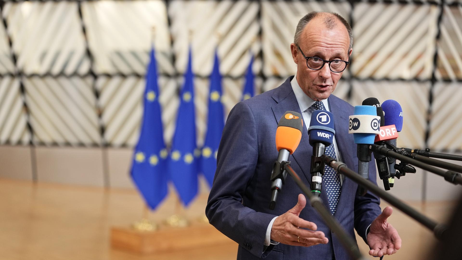 Bundeskanzler Merz steht vor einer Reihe von Mikrofonen. Im Hintergrund sind mehrere Flaggen der Europäischen Union.