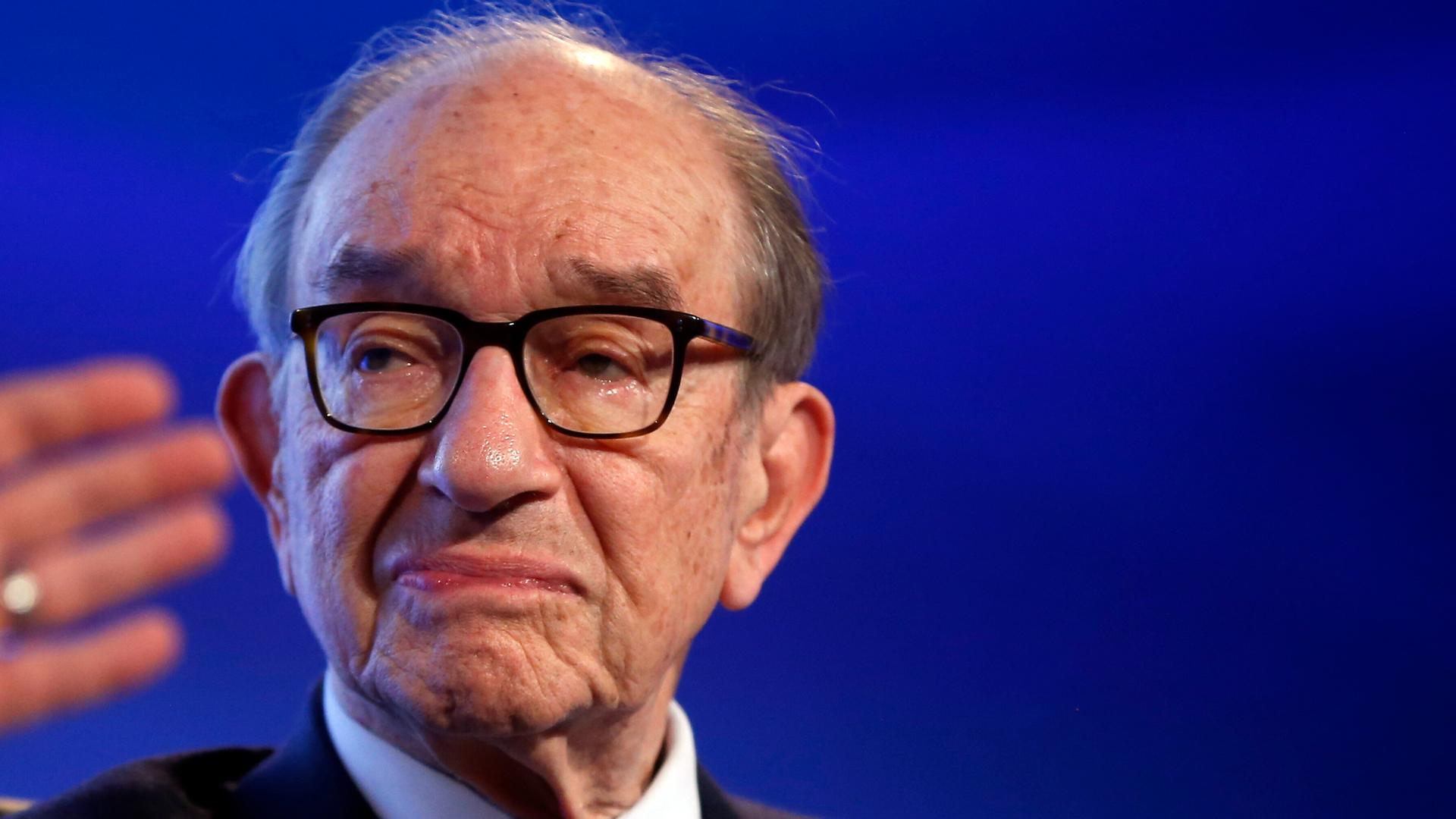 Alan Greenspan im Porträt, rechts von ihm sieht man verschwommen die Hand seines Gesprächspartners.