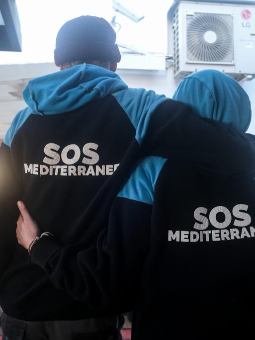 Ein Mann und eine Frau stehen Arm in Arm auf einem Schiff und tragen Anoraks mit der Aufschrift SOS Mediterranee