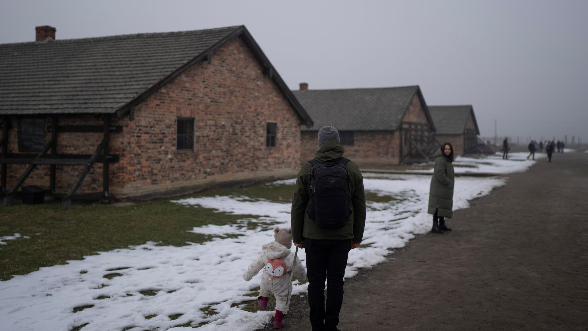 Eine Familie mit kleinem Kind steht vor Häftlingsbaracken im ehemaligen Konzentrations- und Vernichtungslager Auschwitz-Birkenau am 23. Januar. 2025. 