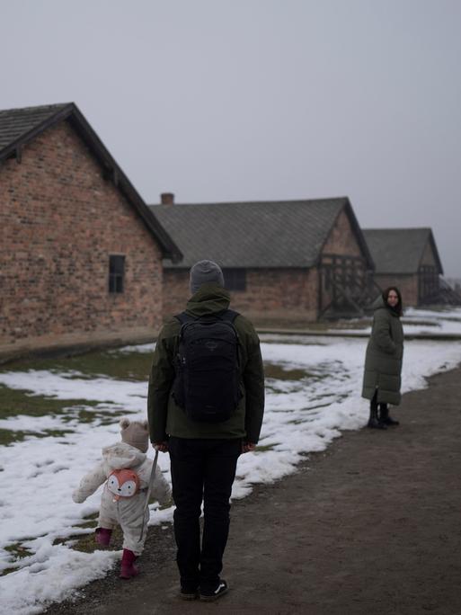 Eine Familie mit kleinem Kind steht vor Häftlingsbaracken im ehemaligen Konzentrations- und Vernichtungslager Auschwitz-Birkenau am 23. Januar. 2025. 