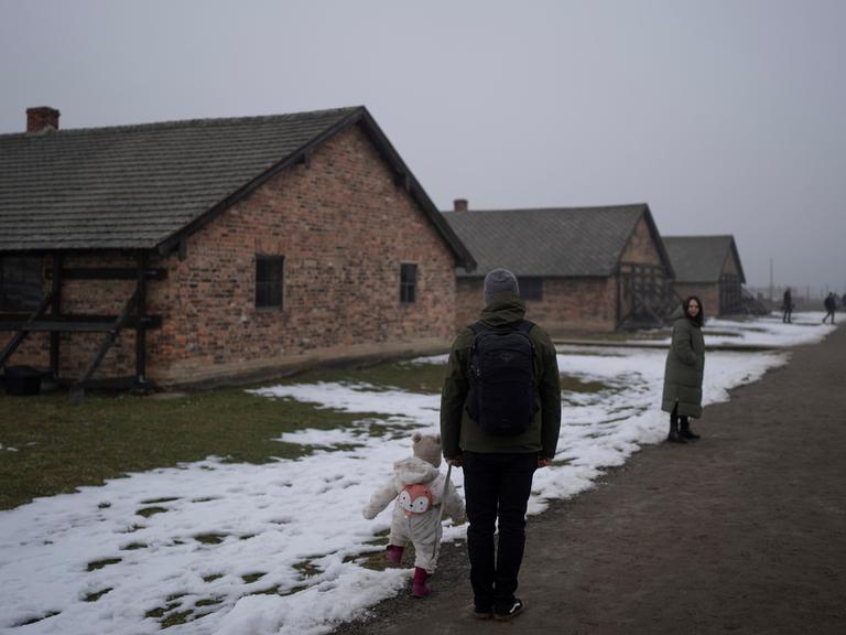 Eine Familie mit kleinem Kind steht vor Häftlingsbaracken im ehemaligen Konzentrations- und Vernichtungslager Auschwitz-Birkenau am 23. Januar. 2025. 