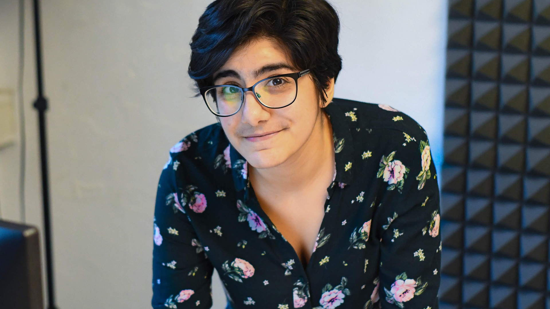 "Dark Agent"-Host Shahrzad Golab mit dunklen, kurzen Haaren, schwarzer Brille und Bluse mit Blumenmuster schaut leicht lächelnd in die Kamera.