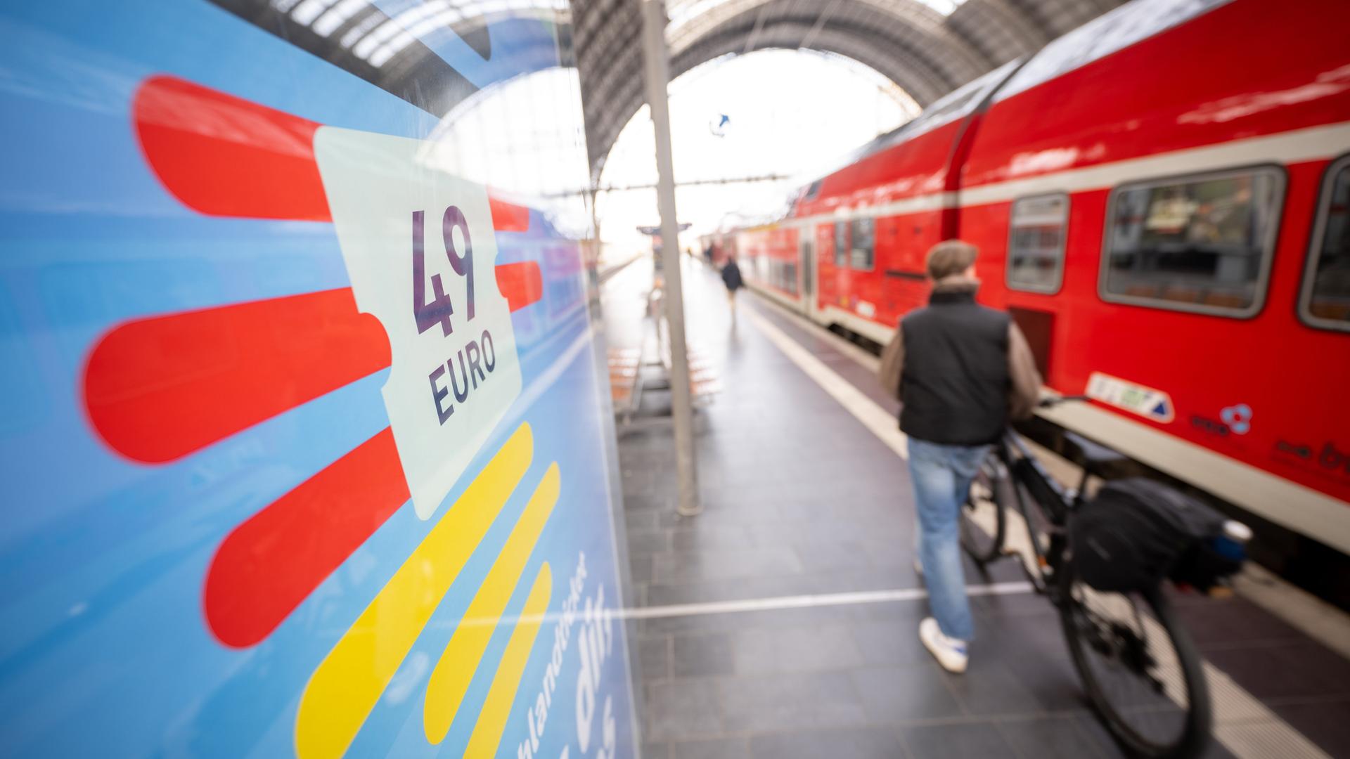Ein Mann geht am Frankfurter Hauptbahnhof mit seinem Fahrrad zwischen Werbung für das Deutschlandticket und einer Regionalbahn entlang.