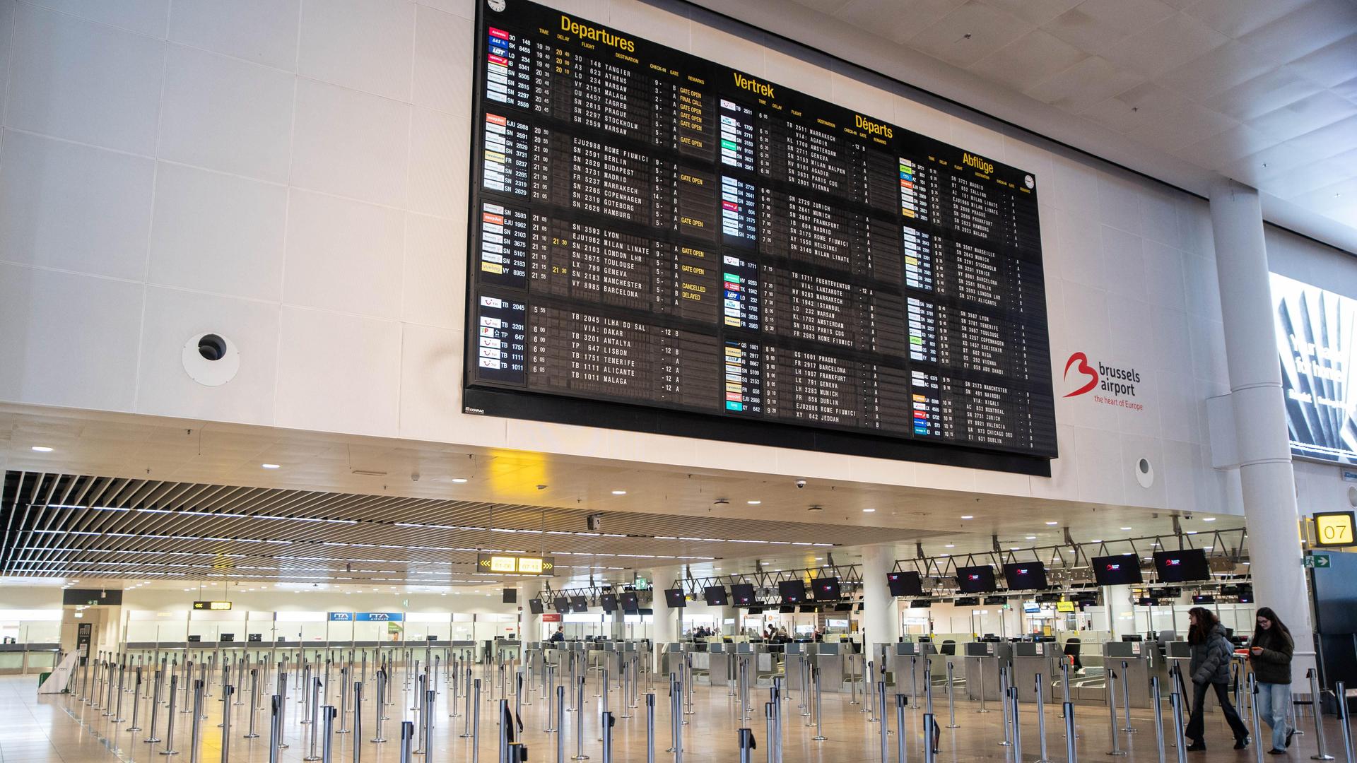 Blick auf die riesige Tafel mit zahlreichen Fluganzeigen an einer weißen Wand. darunter ein breiter Gang. Blick auf die riesige Tafel mit zahlreichen Fluganzeigen an einer weißen Wand. darunter ein breiter Gang.