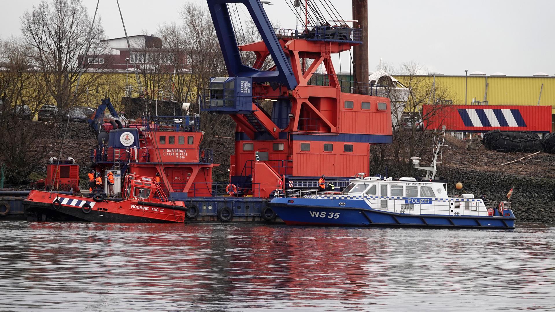 Ein Schiff der Wasserschutzpolizei hält neben einem Kran, der ein gesunkenes Schiff in der Nähe der Köhlbrandbrücke geborgen hat.