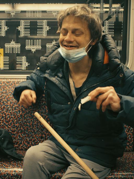 Im Still aus "Hausnummer Null" sitzen zwei Männer mit Bierflaschen nebeneinander in der U-Bahn und lachen miteinander.