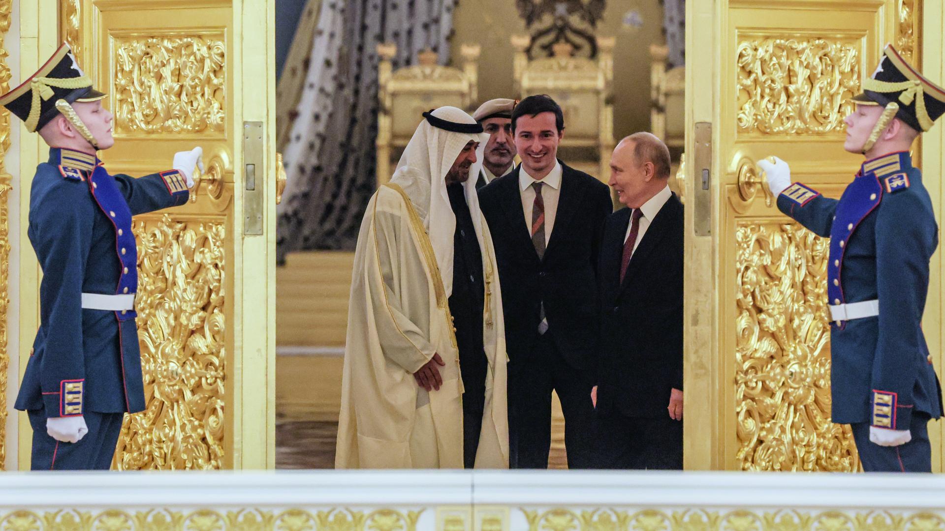 Der russische Präsident Putin und der Präsident der Vereinigten Arabischen Emirate, Scheich Mohamed bin Zayed Al Nahyan, stehen sich gegenüber und schauen sich an. Ihnen wird von zwei Soldaten eine goldbesetzte Tür aufgehalten.