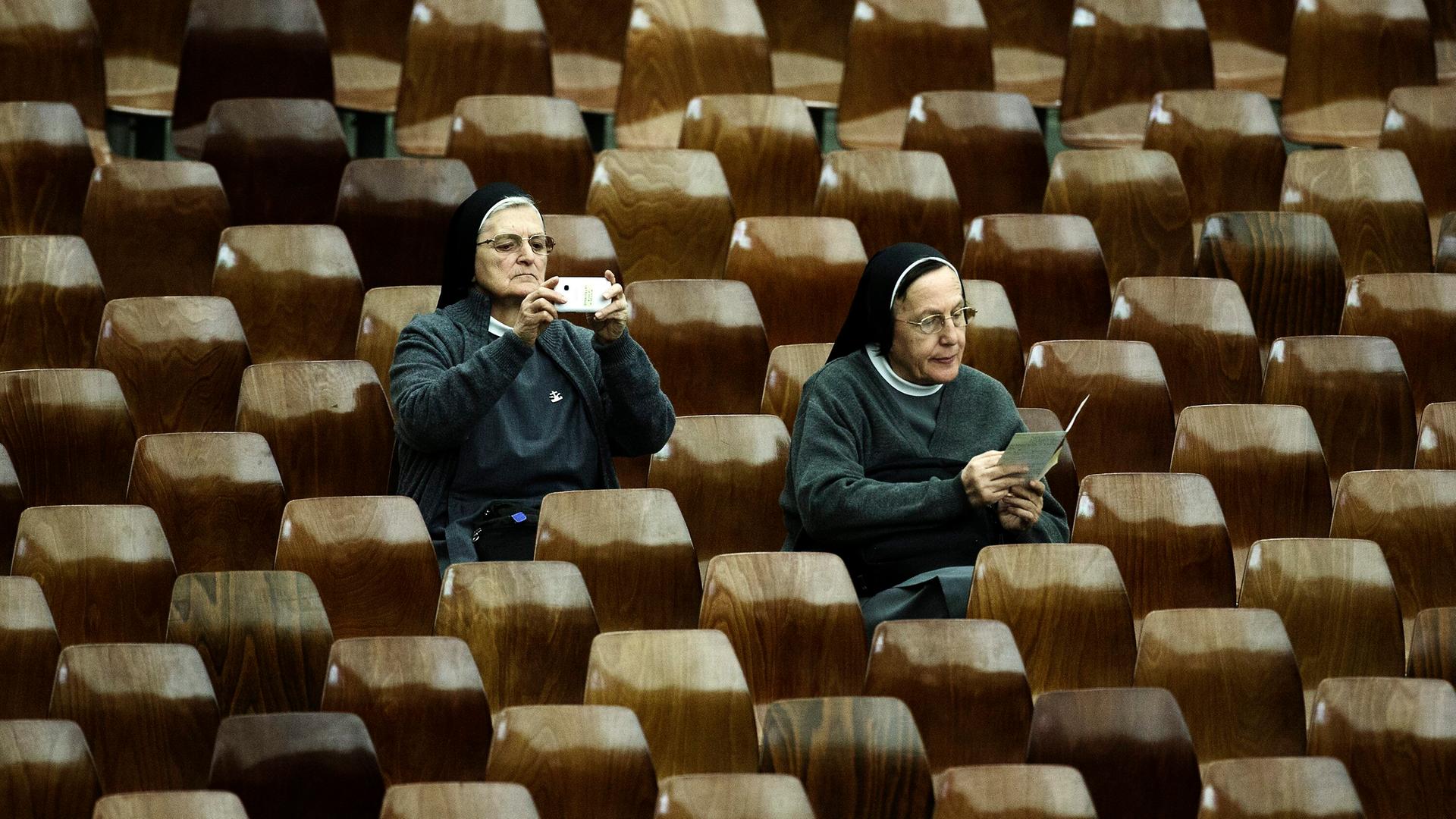 Eine Nonne fotografiert mit ihrem Smartphone  während der Feierlichkeiten zum Jubiläum der Errichtung der Bischofssynode im Vatikan. Schräg vor ihr sitzt eine zweite Nonne, die in einem Flyer blättert. (Symbolbild)