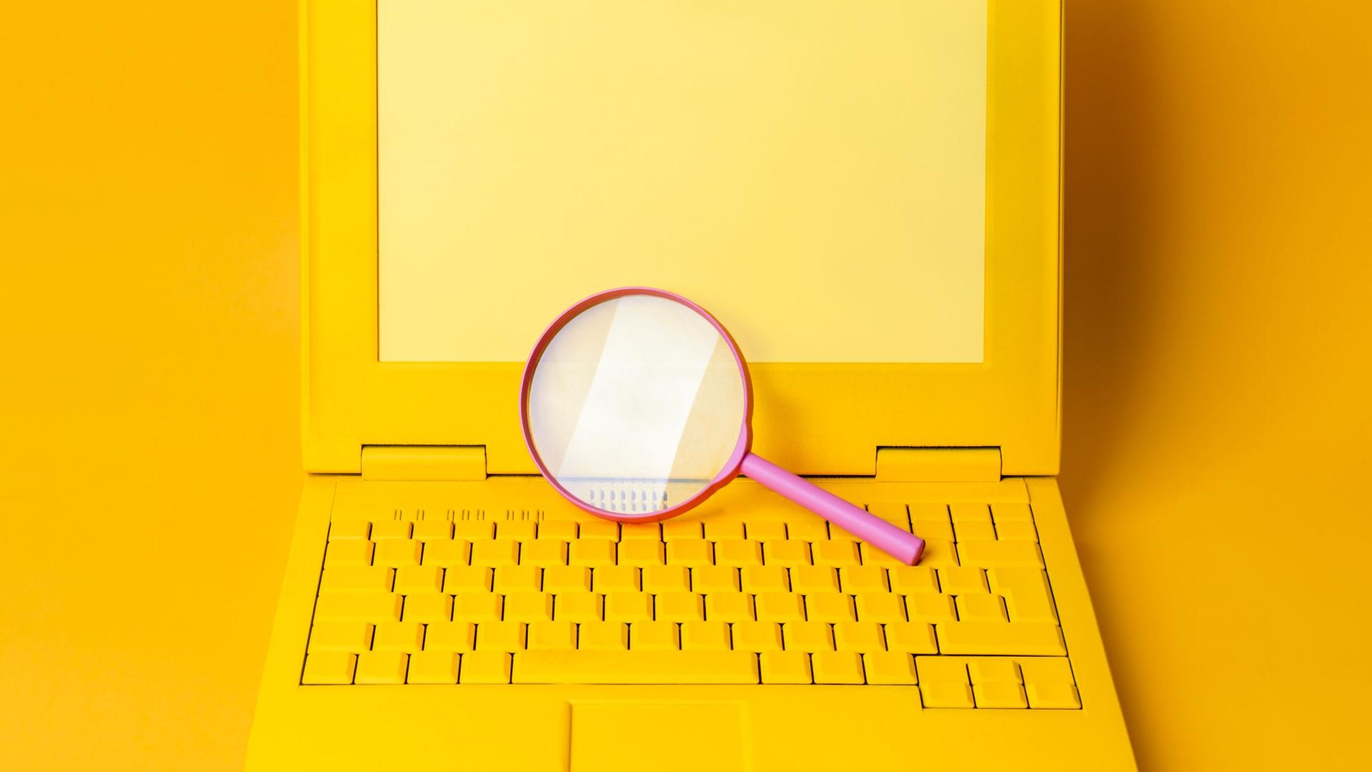 Ein gelber Laptop mit einer Lupe vor gelbem Hintergrund.