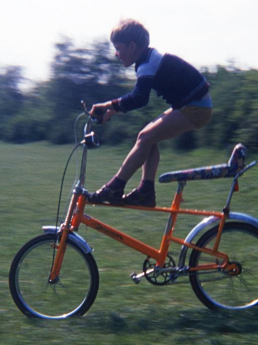 Ein Kind fährt mit einem orangenen Bonanza-Fahrrad über die Wiese.
