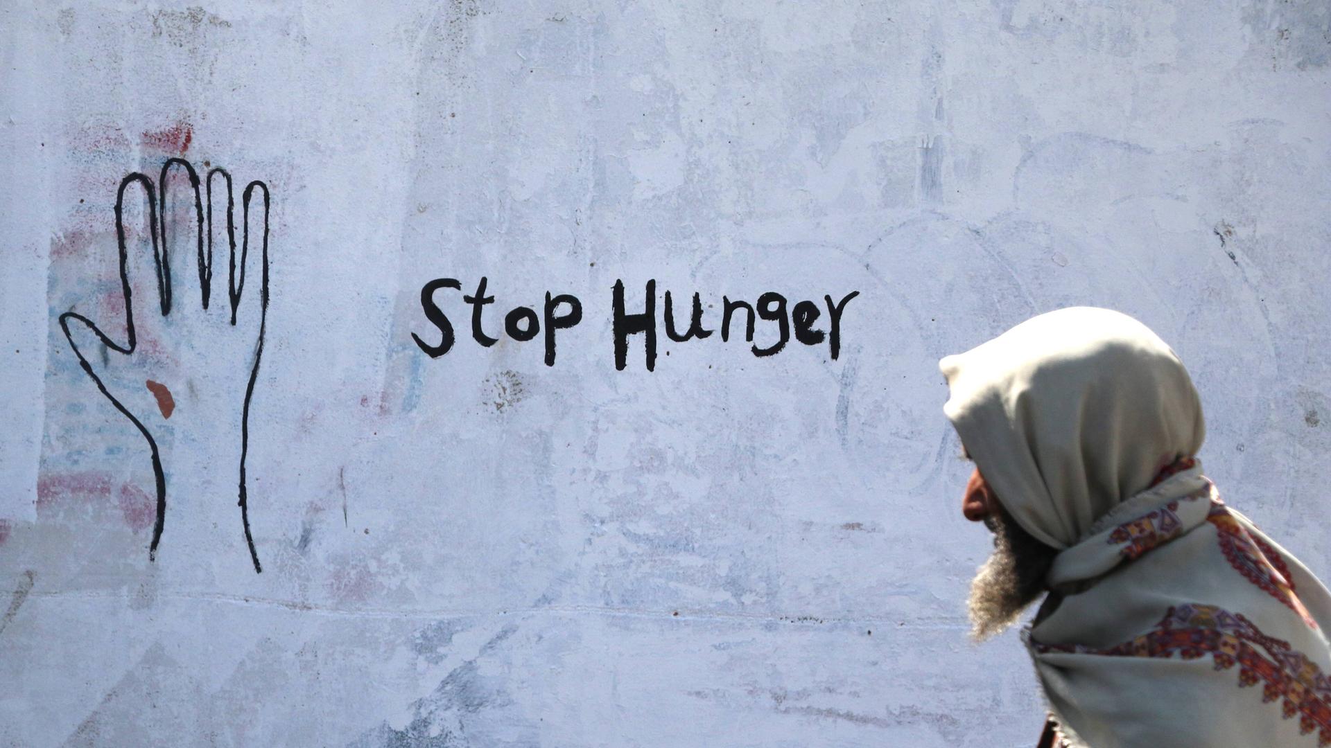 Ein älterer jemenitischer Mann geht an einer Hauswand vorbei, auf der "Stop Hunger" gesprüht ist.
