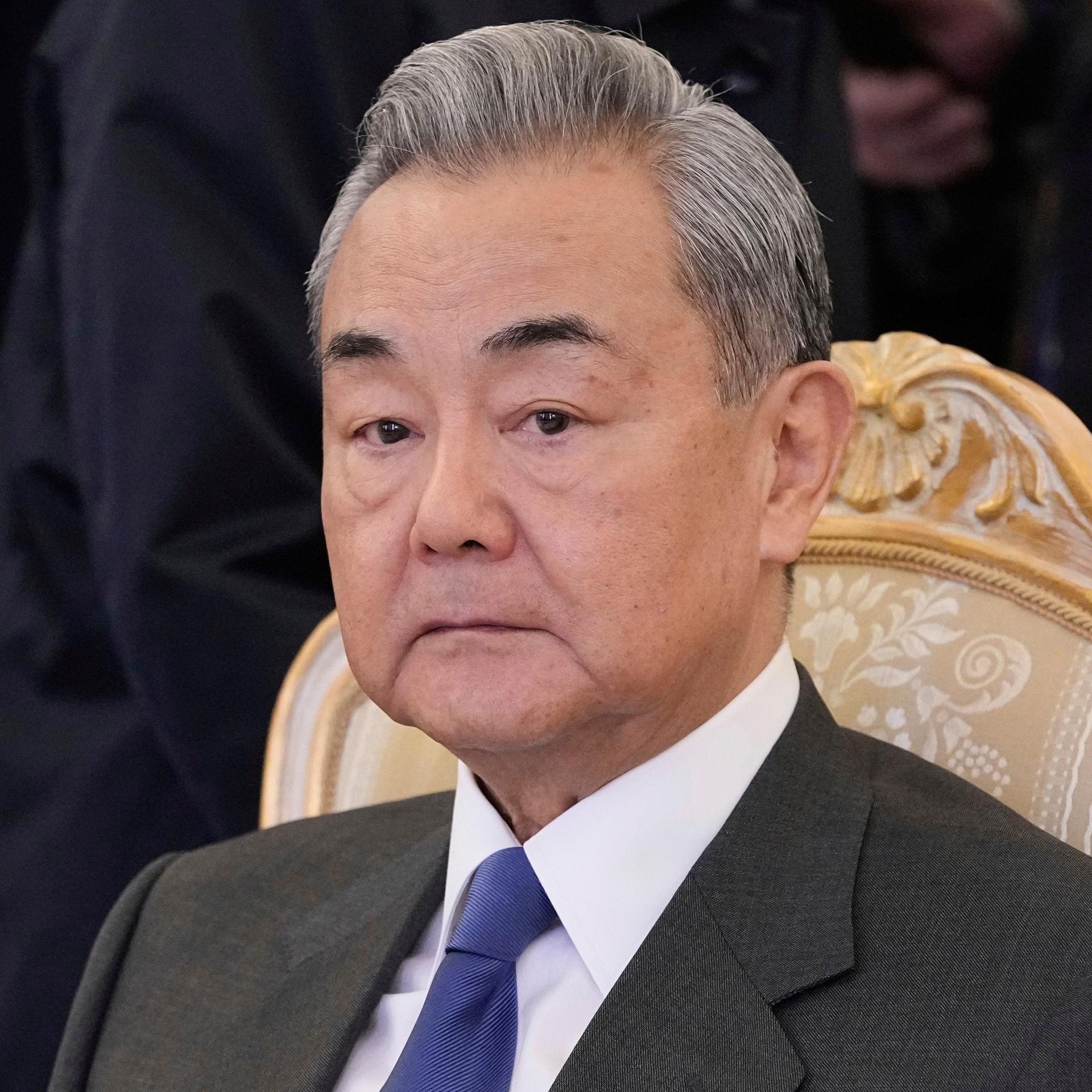 Der chinesische Außenminister Wang Yi sitzt auf einem Stuhl und schaut ernst.