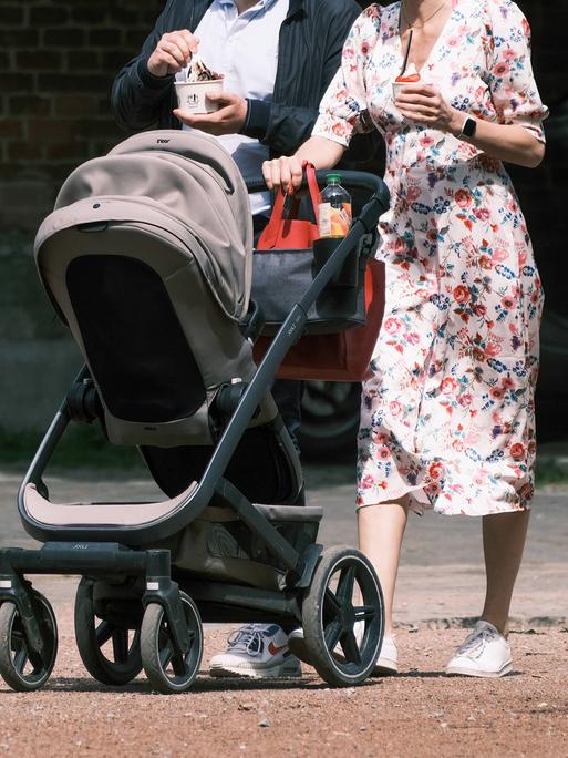 Eine Frau schiebt einen Kinderwagen. Direkt hinter ihr geht ein Mann. 