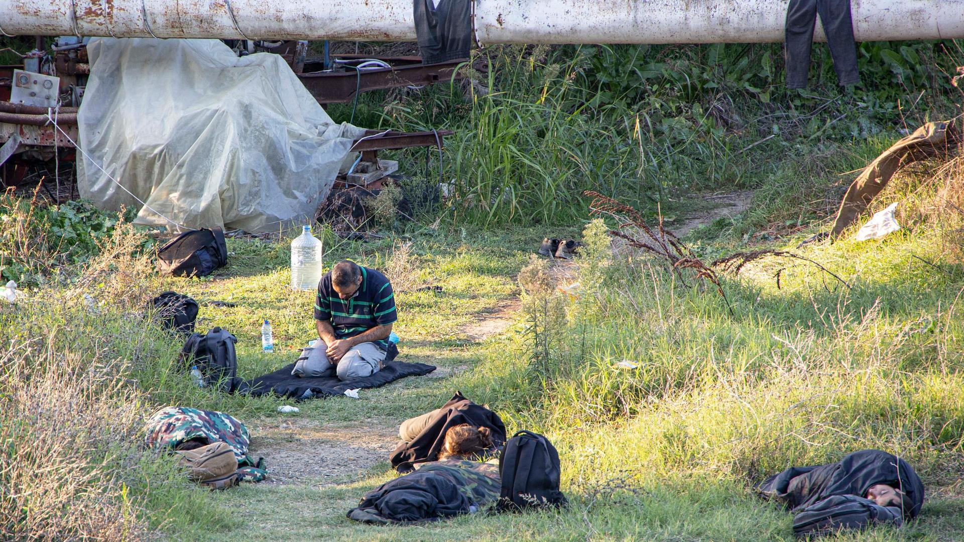 Geflüchtete liegen und sitzen auf dem Gras an der griechischen Grenze.