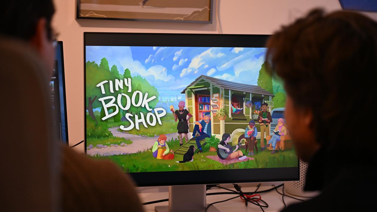 Die Computerspiele-Entwickler David Zapfe-Wildemann (l) und Raven Rusch von dem Kölner Independent-Gamingstudio Neoludic sitzen in ihrem Büro vor einem Bildschirm, auf dem die Startseite des Spiels Tiny Bookshop zu sehen ist. 