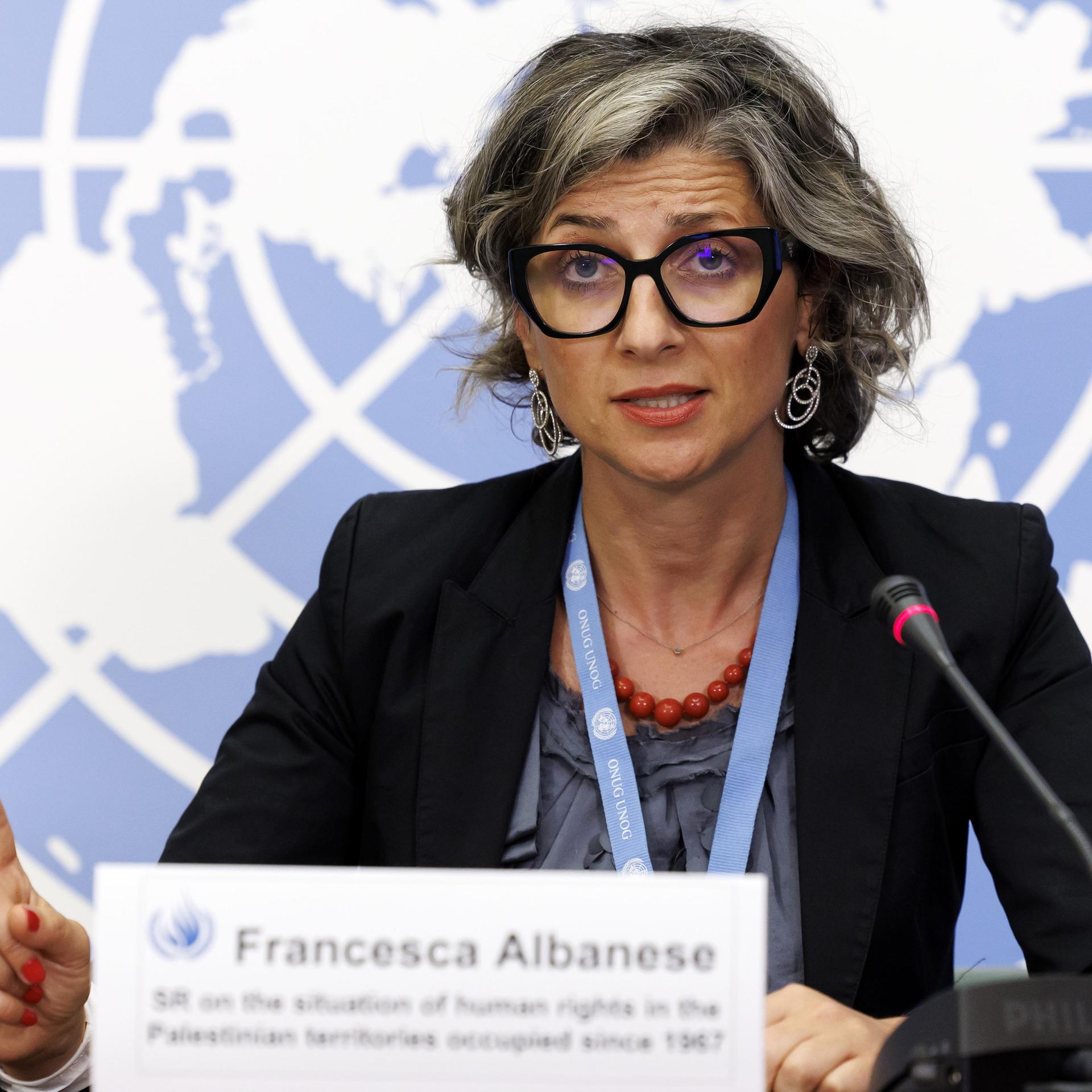 Francesca Albanese sitzt an einem Tisch, spricht in ein Mikrofon und hebt dabei den Zeigefinger der rechten Hand. Im Hintergrund ist eine Weltkarte zu sehen. Francesca Albanese sitzt an einem Tisch, spricht in ein Mikrofon und hebt dabei den Zeigefinger der rechten Hand. Im Hintergrund ist eine Weltkarte zu sehen.