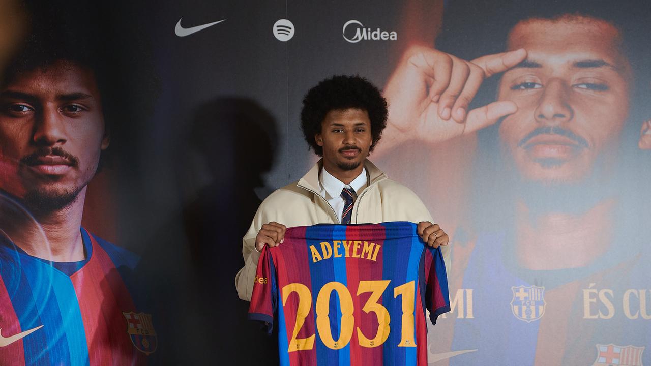 Karim Adeyemi steht bei seiner offiziellen Vorstellung als Spieler des FC Barcelona auf der Bühne. Er hält ein Trikot seines neuen Vereins in den Händen. 
