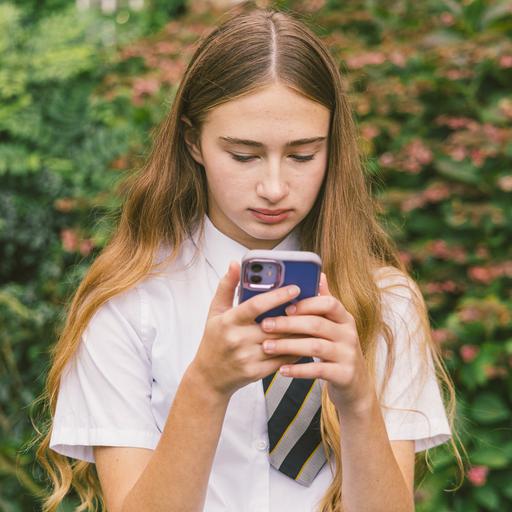 Eine Schülerin in Schuluniform die ernst guckt und auf ihr Smartphone mit bunter Hülle schaut. 