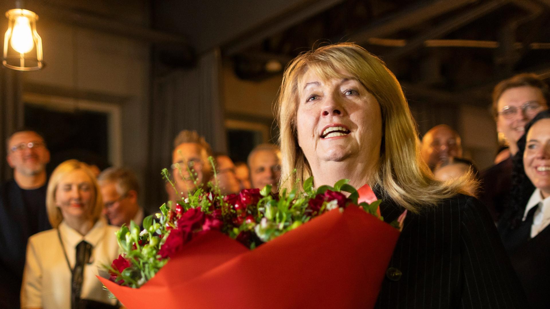 Eine Frau mit blonden Haaren hält einen Strauss rote Rosen.