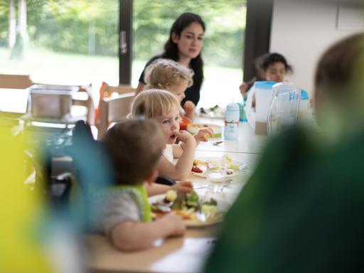 Kinder und Betreuungspersonal in einer Kita beim gemeisamen Mittagessen.
