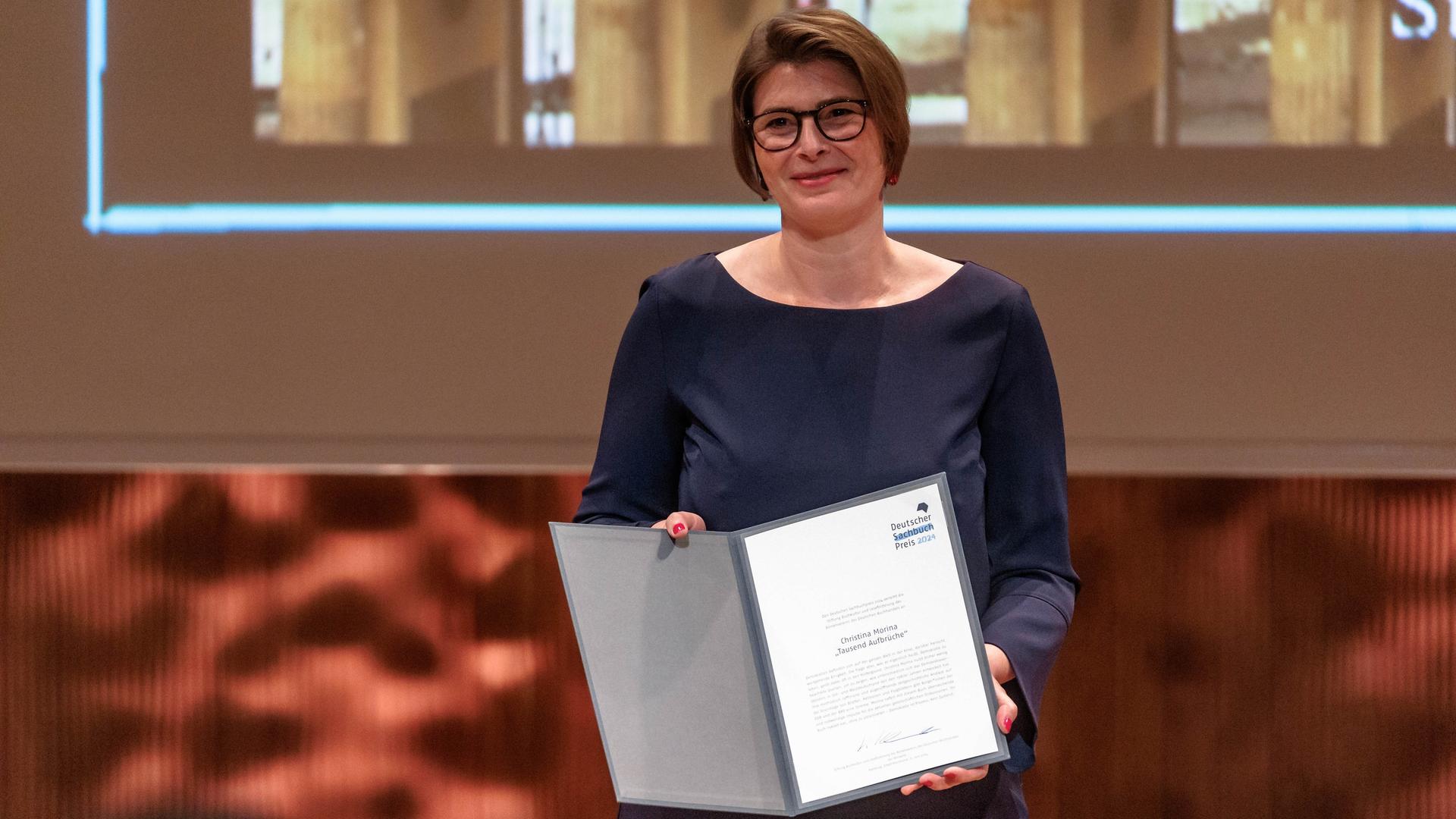 Die Autorin Christina Morina zeigt die Urkunde des Deutschen Sachbuchpreis 2024, den sie für ihr Buch "Tausend Aufbrüche" erhalten hat. 