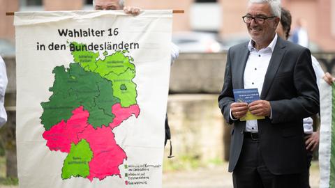 Roger Lewentz, Vorsitzender der SPD Rheinland-Pfalz, während einer Demonstration im Jahr 2023 für die Absenkung des Wahlalters auf 16 Jahre. Neben sich eine Karte der Bundesländer mit den unterschiedlichen Altersgrenzen.