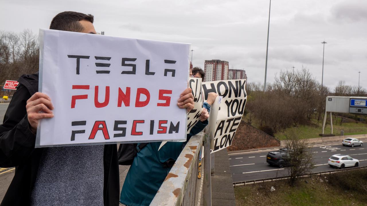 Demonstranten halten Schilder auf einer Brücke über einer Straße hoch, darauf steht: "Tesla funds fascism" oder "honk if you hate Elon".