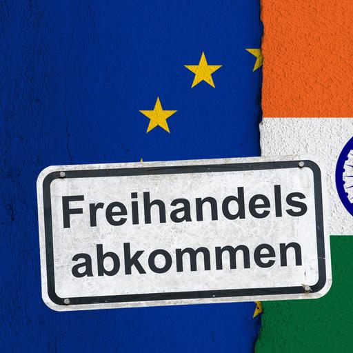 Ein weißes, verwittertes Hinweisschild mit der Aufschrift "Freihandelsabkommen", befestigt mit Schrauben an einer Wand mit der Flagge der Europäischen Union und der Nationalflagge der Republik Indien.