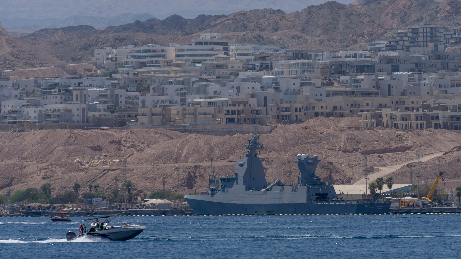 Ein graues Militärschiff liegt vor einer Hafenstadt vor Anker.
